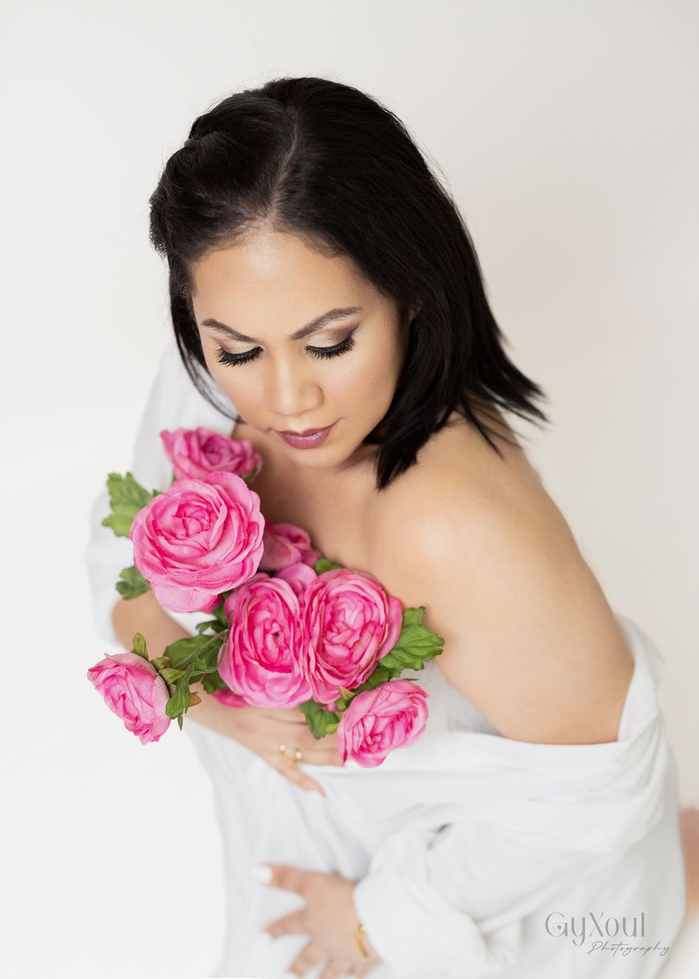 Artistic portrait with bright pink roses against white fabric in soft, romantic lighting.