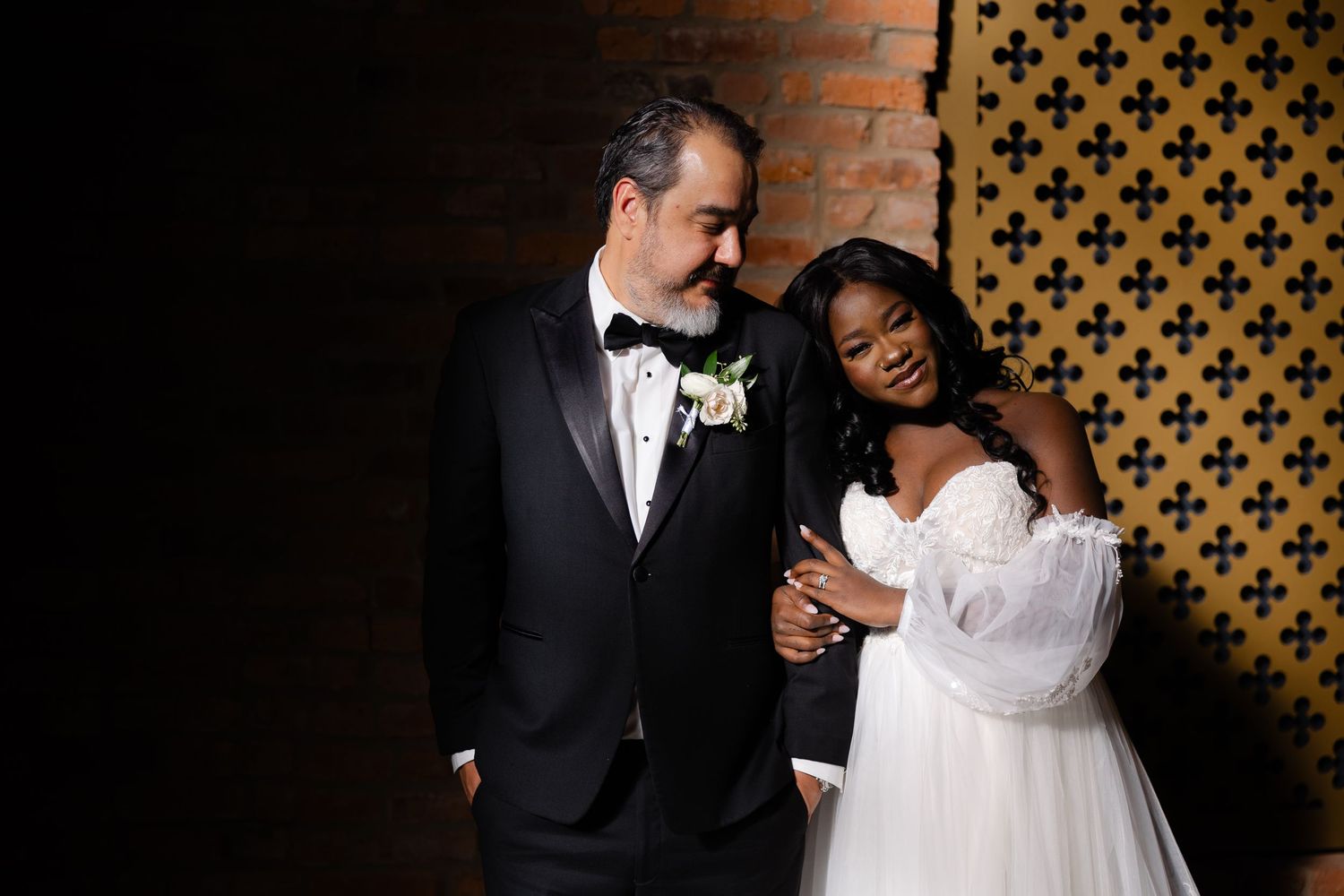 A romantic couple in formal wedding attire share intimate moments against a decorative patterned wall.