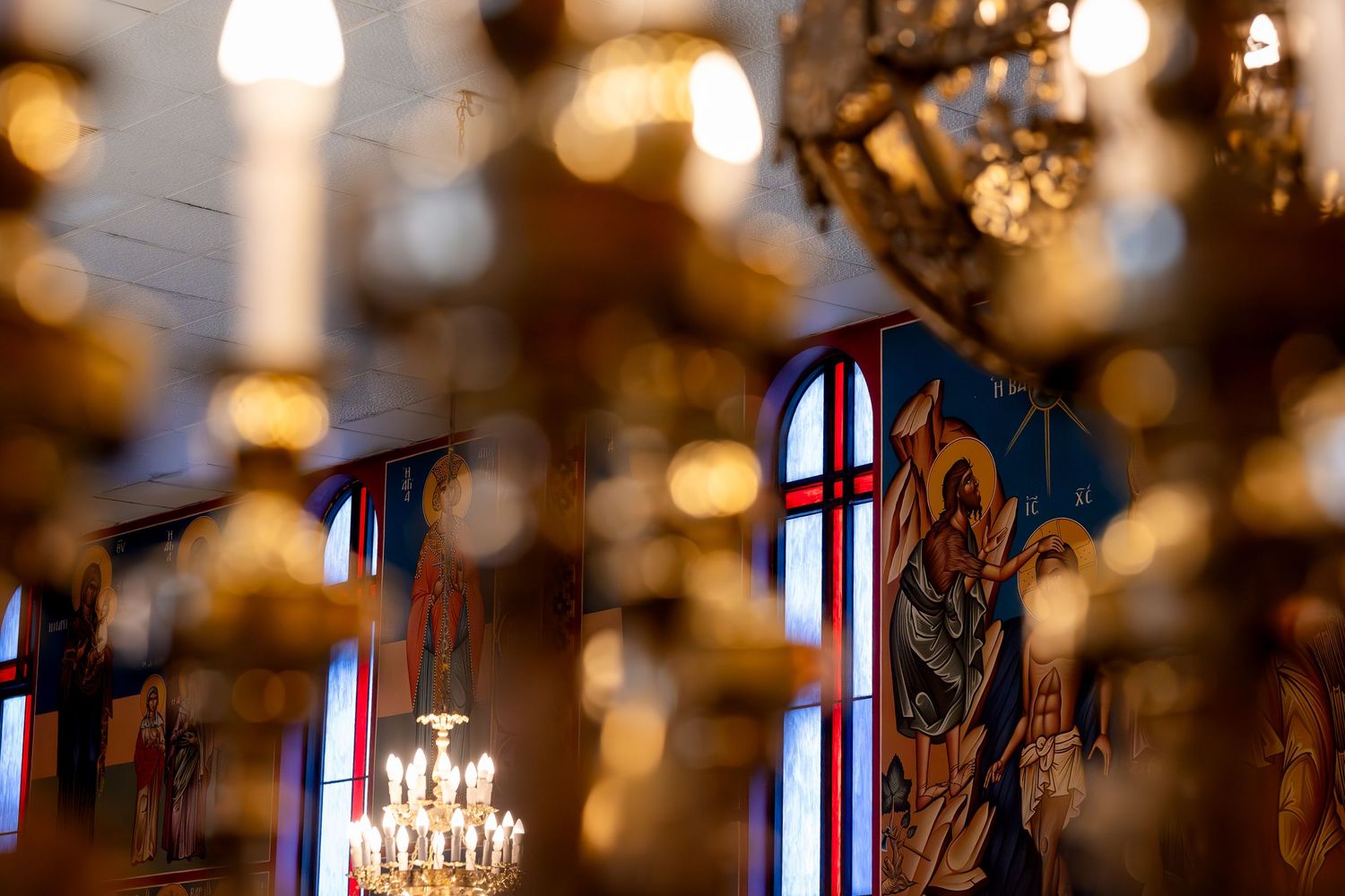 Golden chandeliers and Byzantine religious murals illuminate the ornate interior of an Orthodox Christian church.