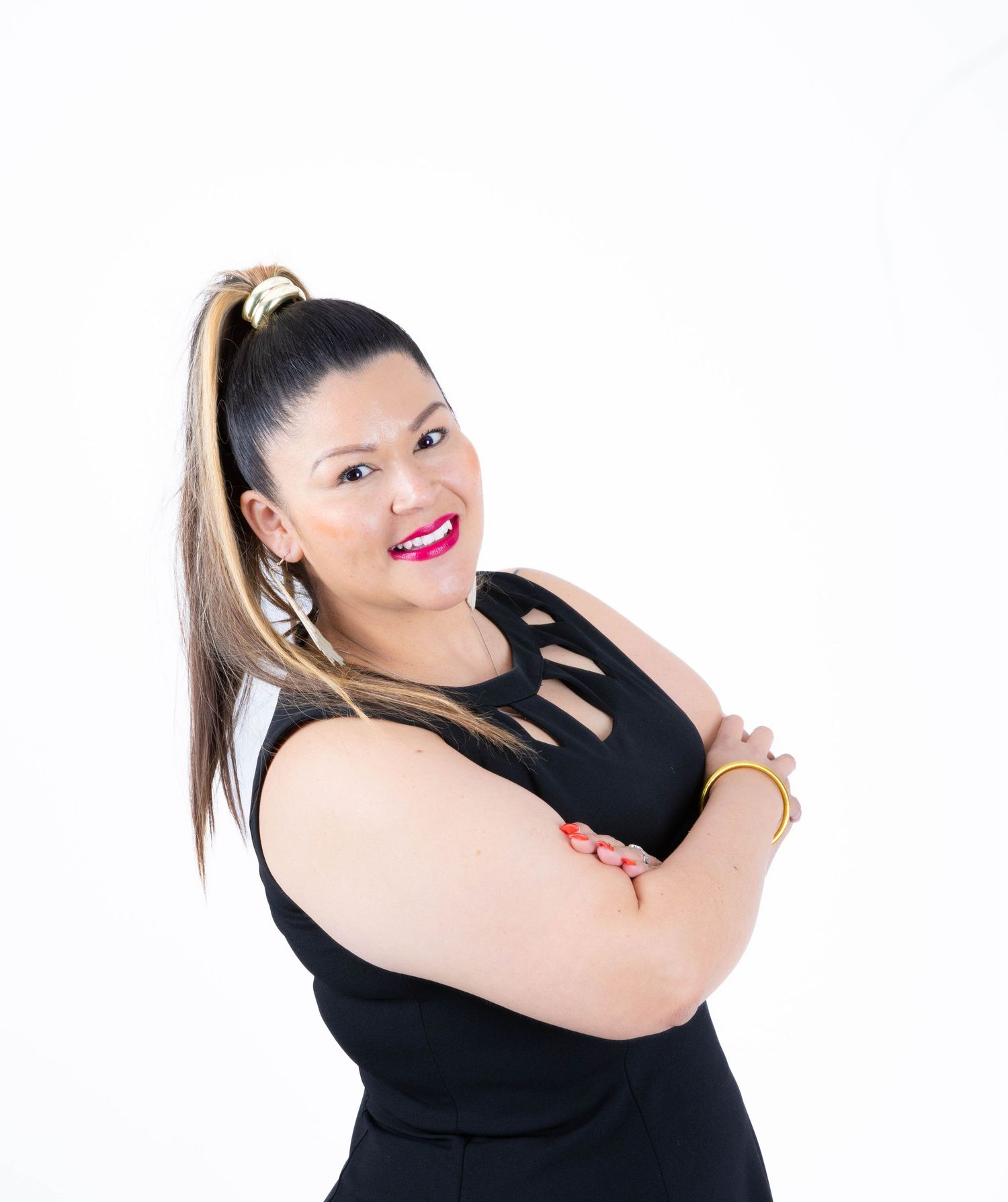 A person wearing a black sleeveless top with cutout details poses confidently against a white background with a bright smile.