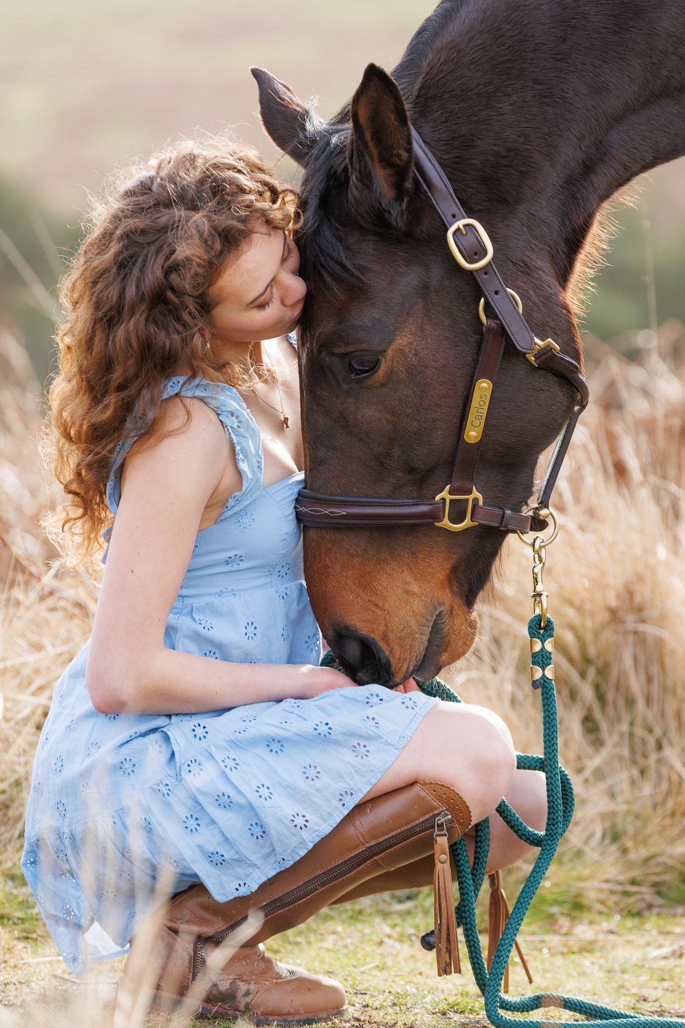 A person in a pink sweater and jeans stands with a black horse against a backdrop of golden autumn foliage.