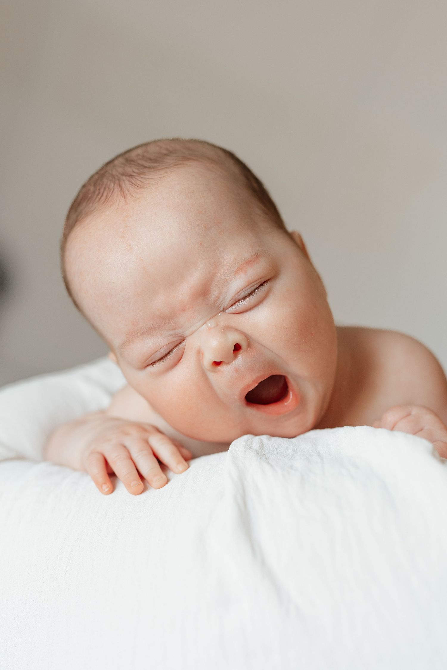 A sleeping newborn baby lies peacefully on white bedding in a series of close-up shots showing their peaceful expression.