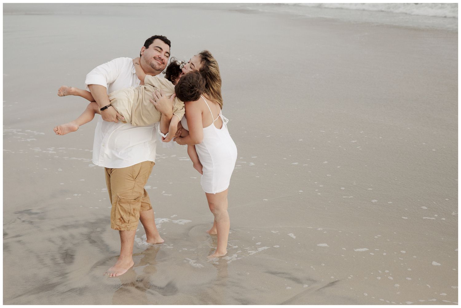 A joyful couple dances together on a scenic beach during a romantic photoshoot at sunset.