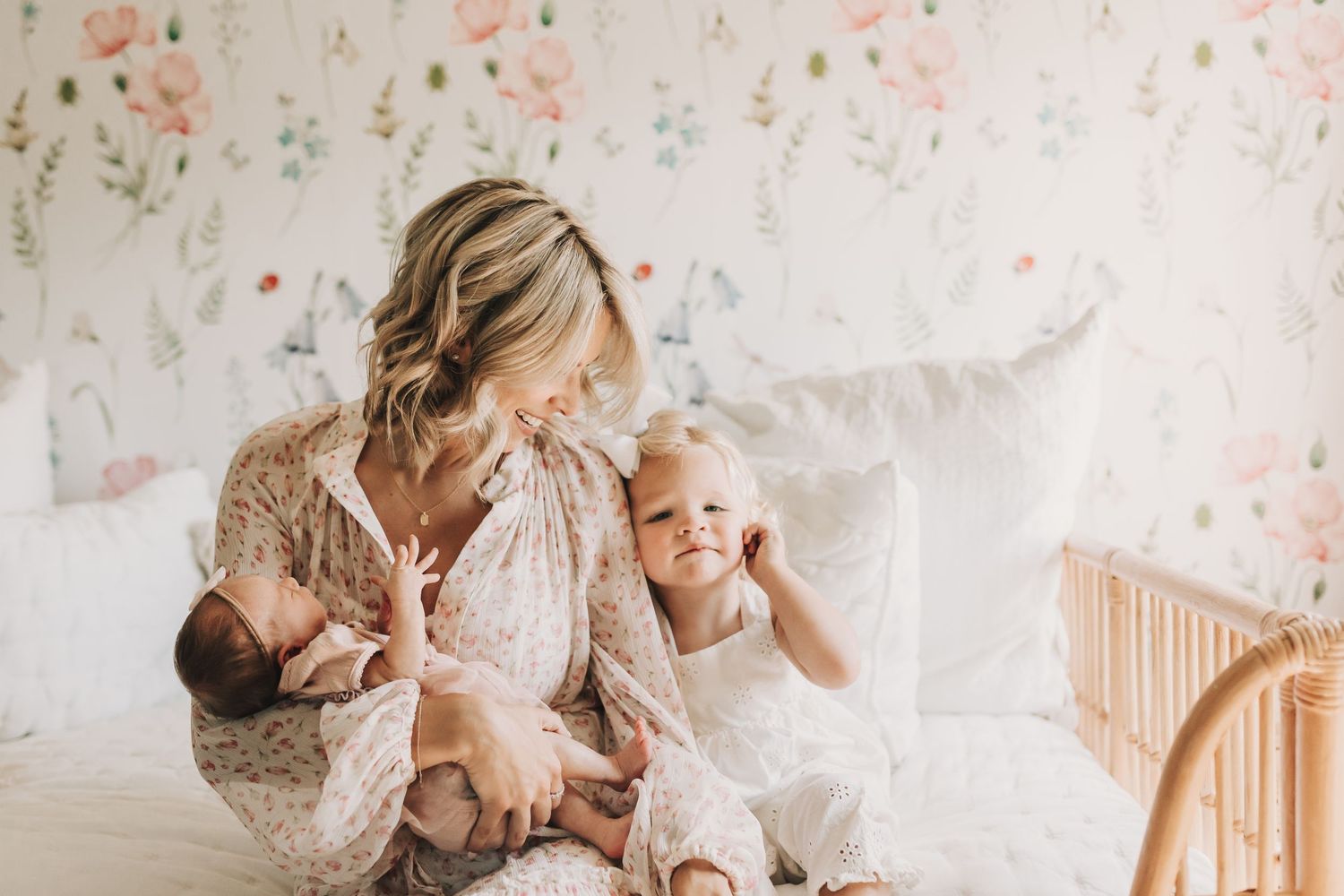 A tender moment between parent and child sitting on a bed with floral wallpaper in soft natural lighting.