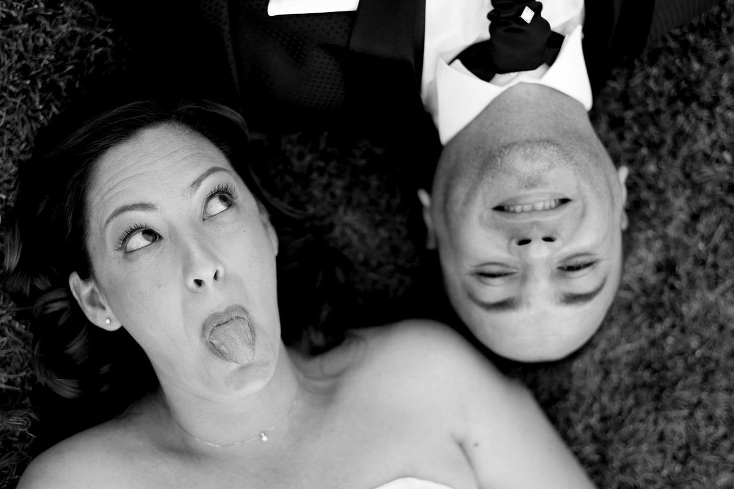 Brautpaar liegt im Gras, Braut schneidet eine Grimasse: Be yourself und 'no fake' Hochzeitsfotografie in NRW