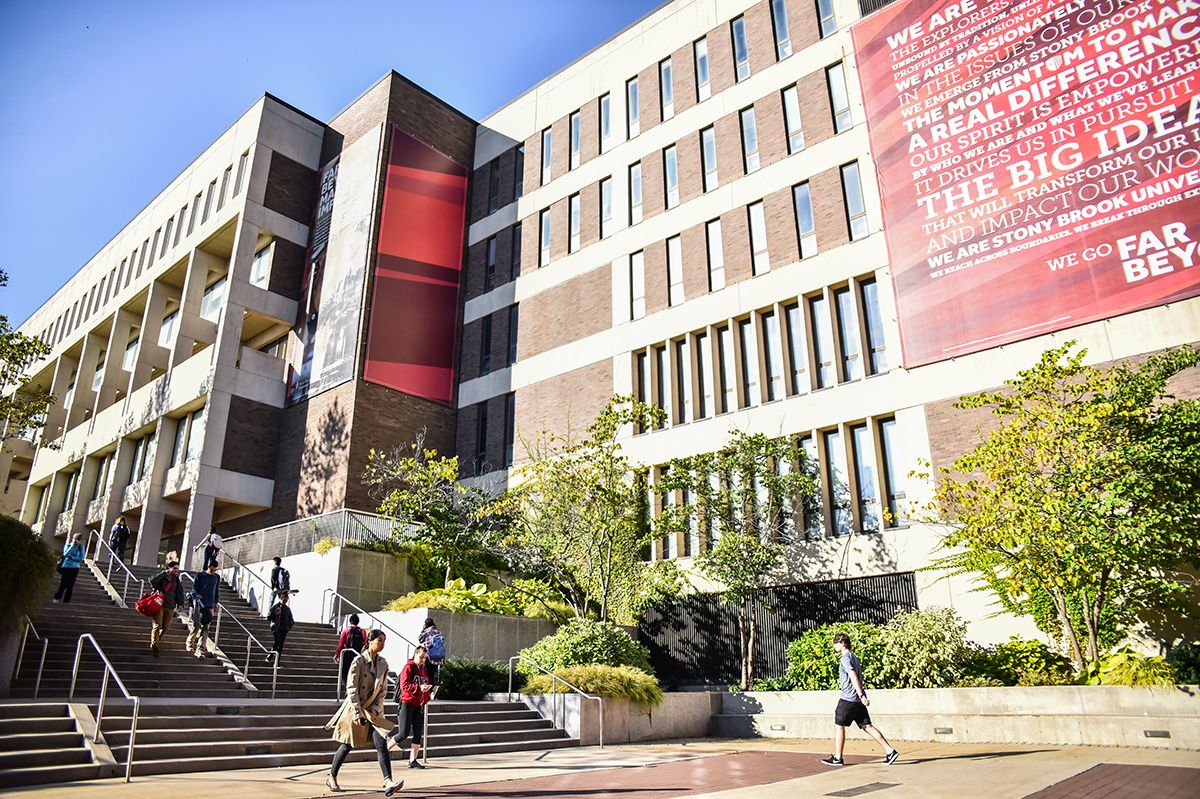 Modern university campus buildings with red architectural accents against a bright blue sky.