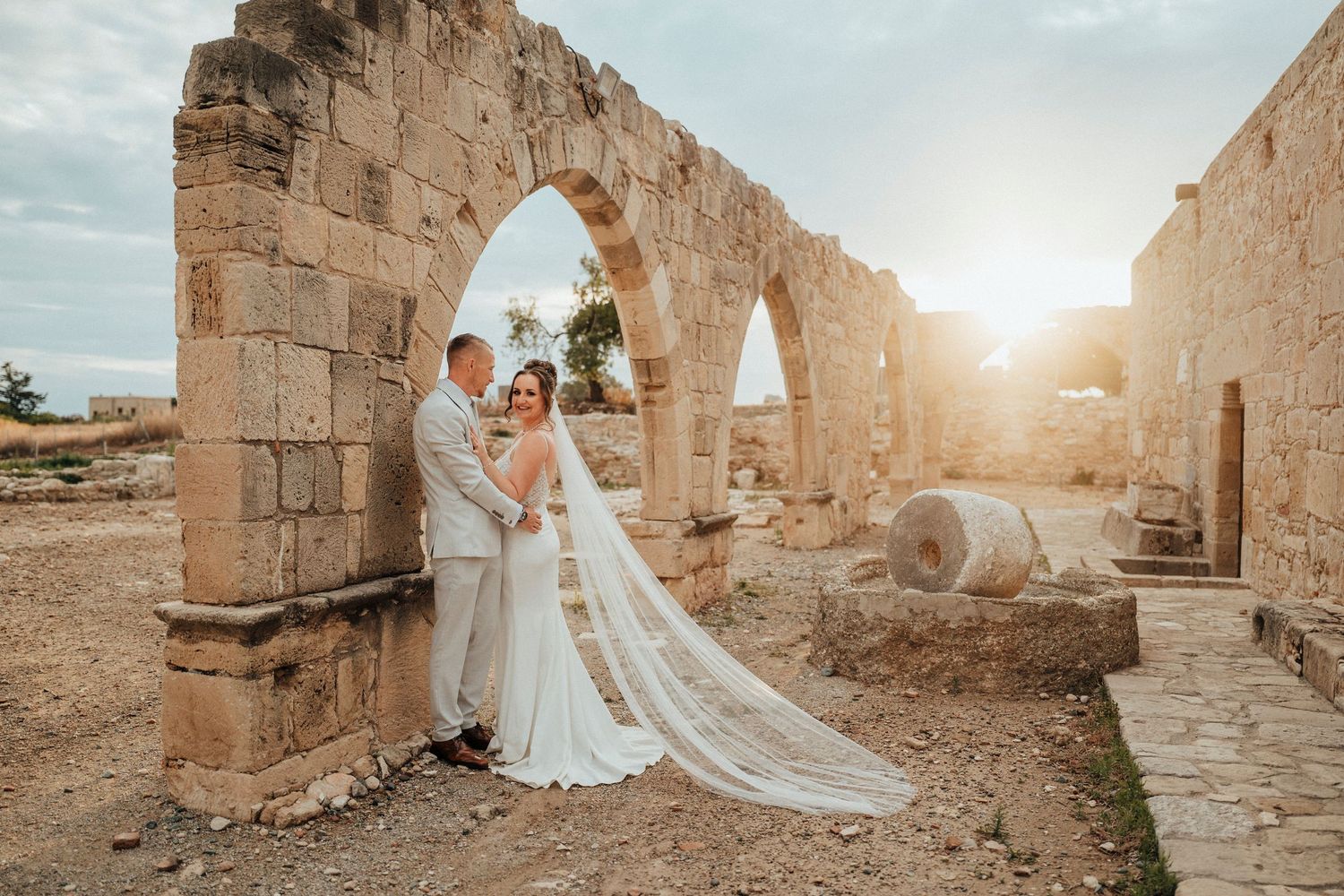 A romantic wedding moment captured among lush greenery with two people embracing in formal attire.