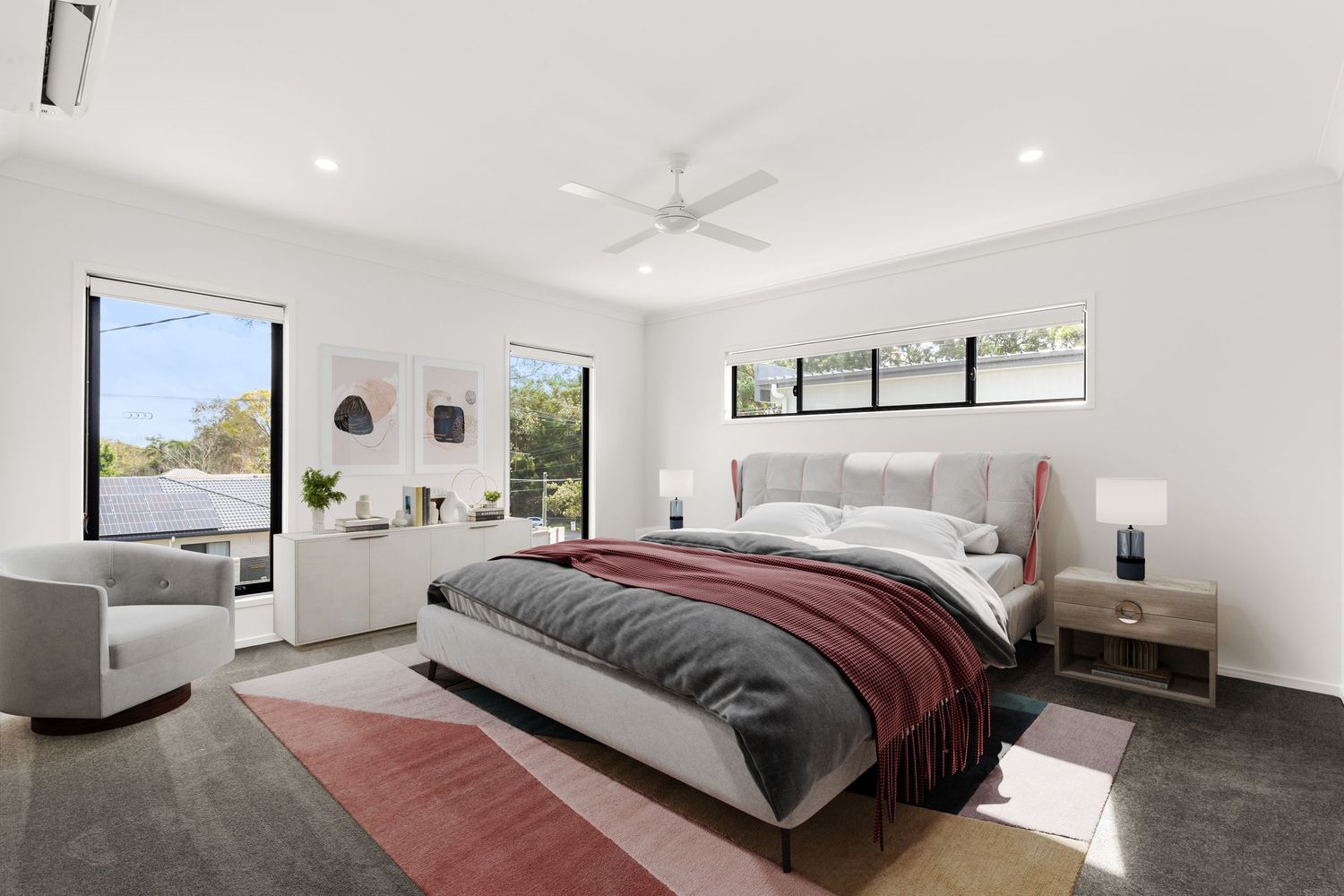 Spacious master bedroom with upholstered bed, ceiling fan, large windows, and stylish pink and grey area rug.
