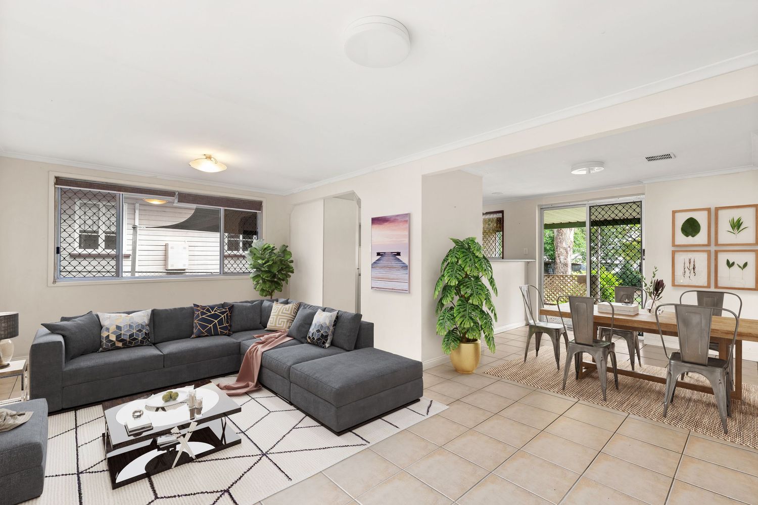 Open-plan living and dining area with grey sectional sofa, tiled floors, and kitchen visible in background.