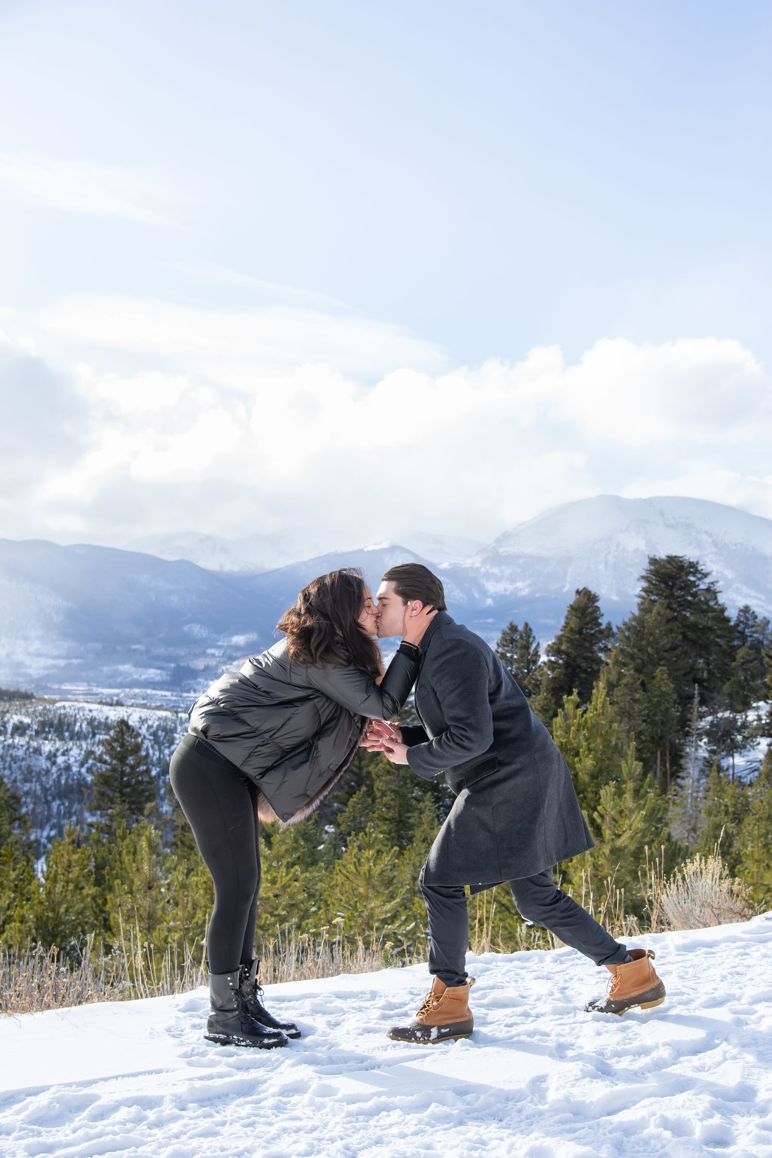 A couple shares a romantic kiss in the snow with scenic mountain views during winter proposal at Sapphire Point Breckenridge Colorado
