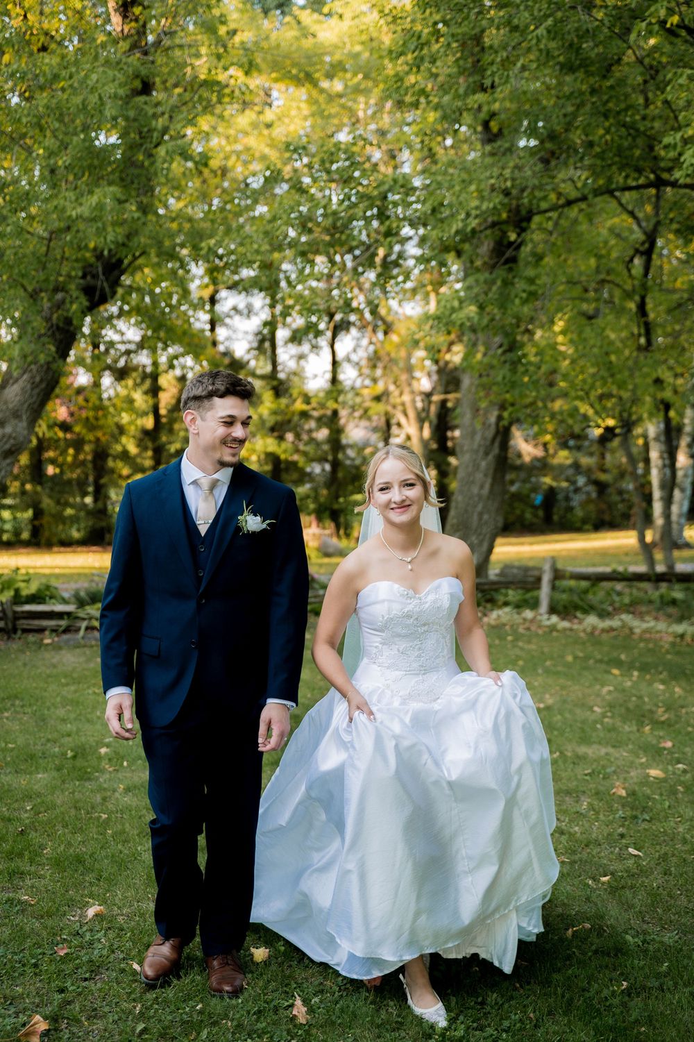 A wedding couple poses playfully in a lush autumn park setting with golden foliage.