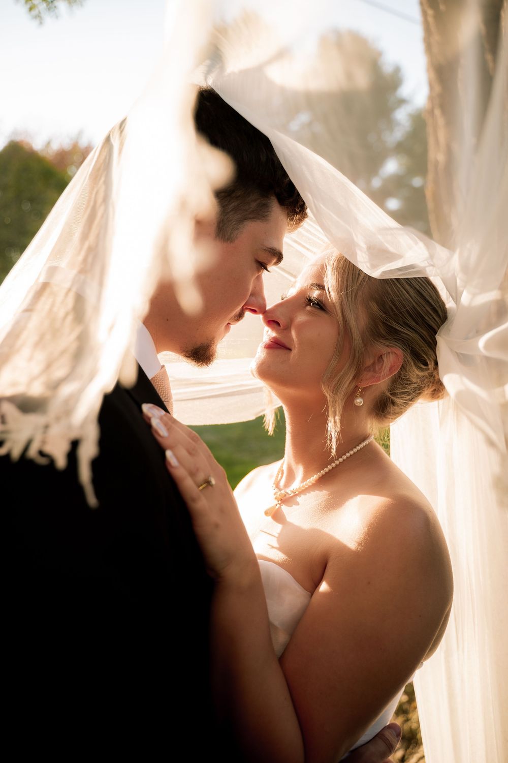 Romantic wedding couple shares intimate moments under flowing white veils in a series of artistic portraits.