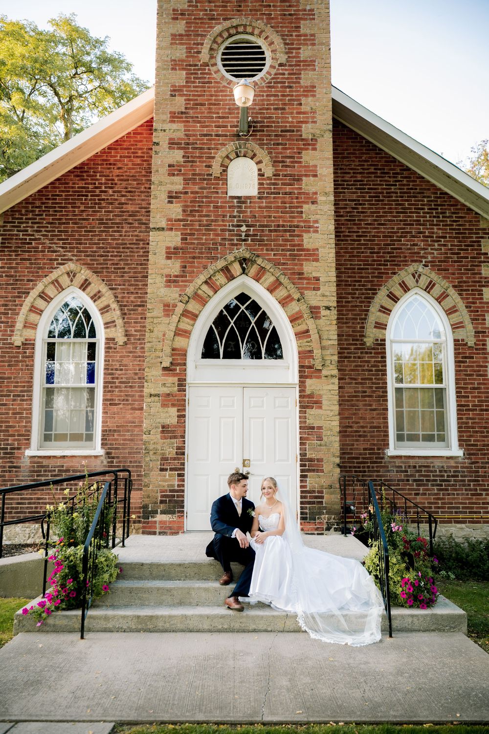 Wedding couple poses in sequence outside historic brick church with gothic windows.