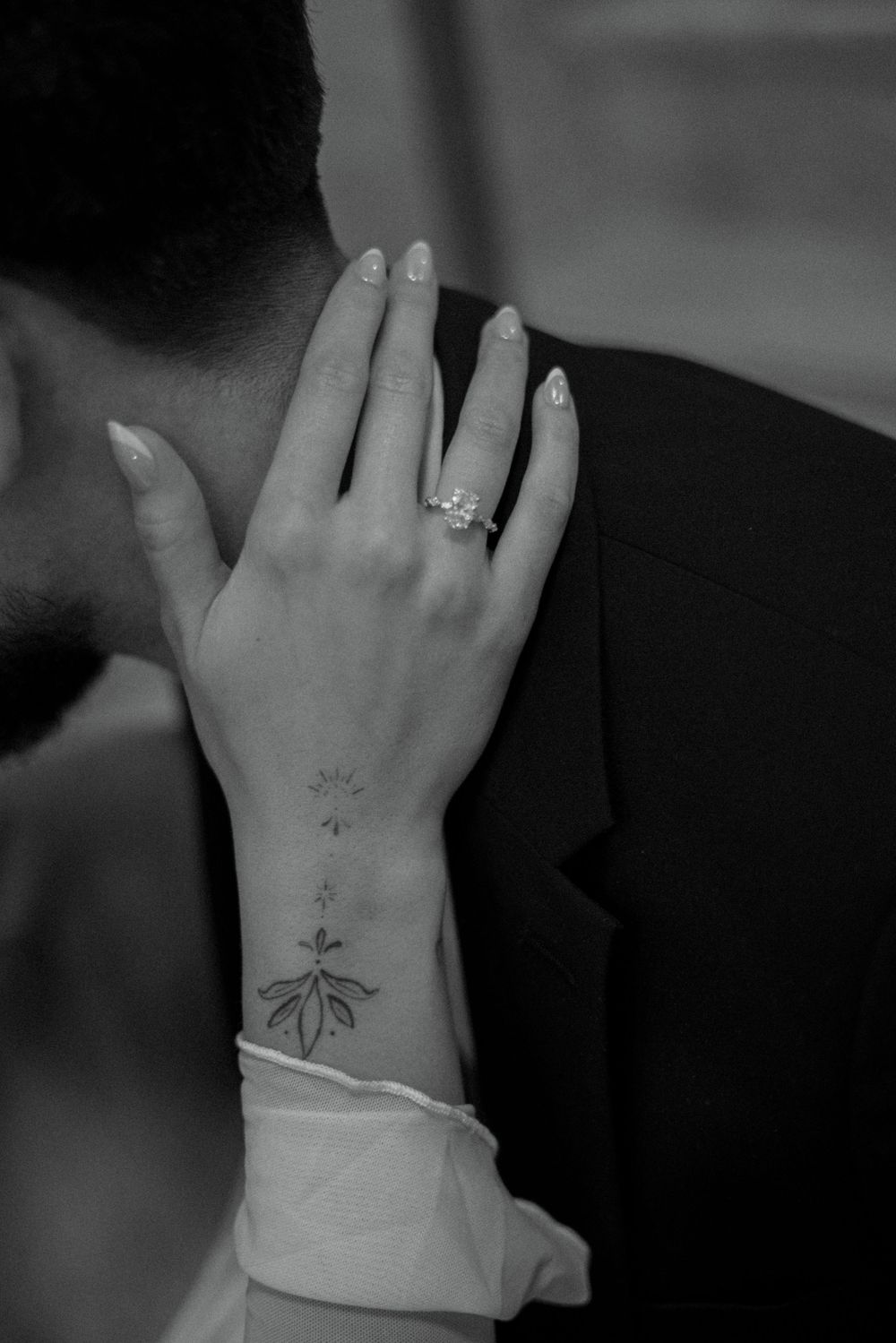 Black and white close-up of brides hand with engagement ring and wrist tattoo.
