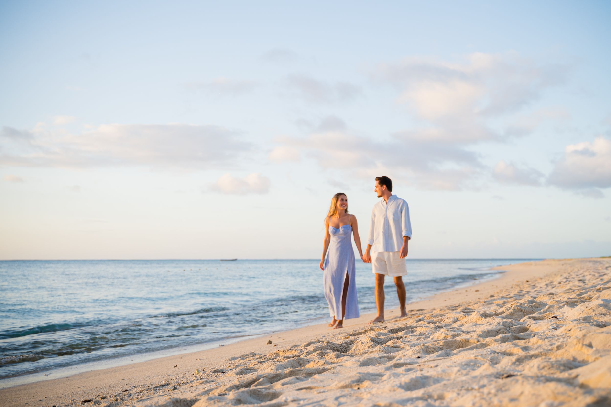 Couple strolling hand in hand on pristine beach at sunset.
