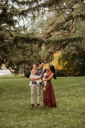 Family enjoying playful moments together on a grassy hill under evergreen trees in autumn.