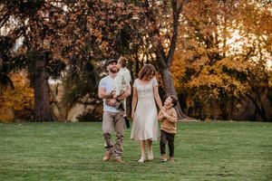 Family enjoying a playful moment together in a park during golden hour with autumn trees in the background.