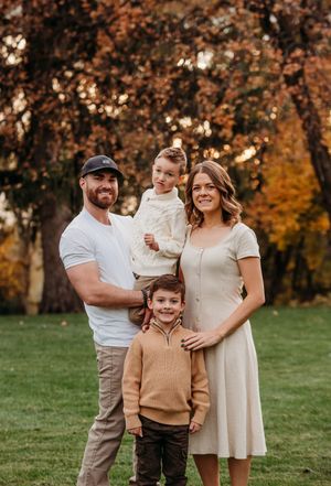 Family wearing neutral tones poses together outdoors during autumn with colorful fall foliage in background.