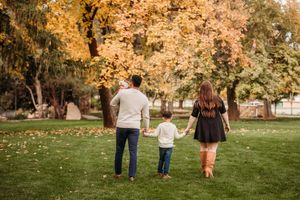 A family walks together on grass under golden autumn trees in a park during a fall photoshoot.