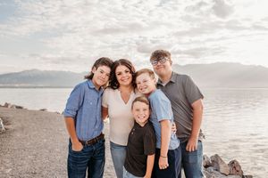 A family enjoys a sunset photoshoot on a scenic beach with mountains and cloudy skies in the background.