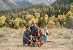 A group enjoys a fall photoshoot in a scenic mountain landscape with golden aspens and evergreen trees in the background.