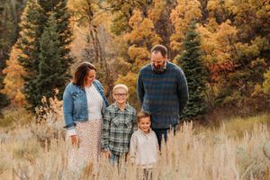 A family walks together through a golden autumn meadow with evergreen trees in the background.