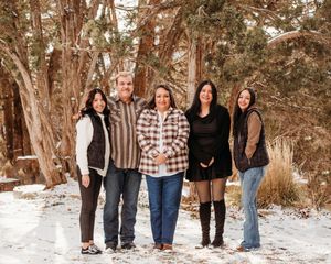 A group of five people standing together on a snowy path with trees in the background.