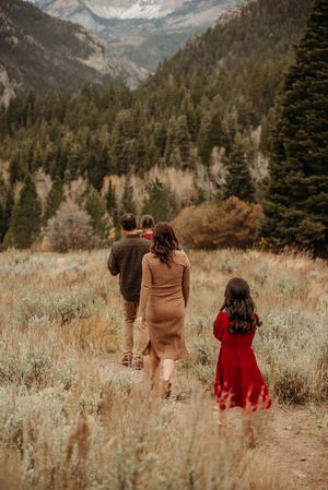 A family walks together through a scenic mountain meadow with snow-capped peaks in the background.