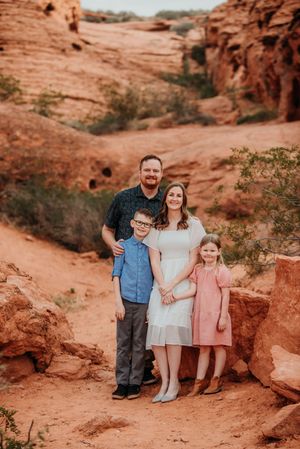 A family poses together on a red rock trail surrounded by towering sandstone formations in the desert landscape.