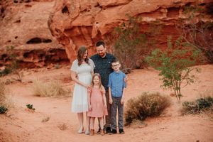 A group stands together against dramatic red rock formations in a desert setting during golden hour.