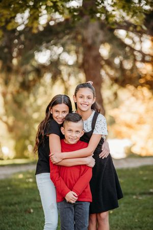 Three children playing and hugging together outdoors in a park during golden hour.