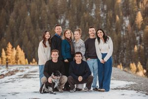 A group poses together on a snowy mountain slope with evergreen trees in the background during golden hour.