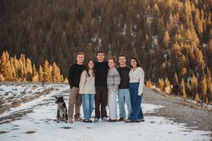 A group of people standing together outdoors in a snowy winter landscape with golden sunlit trees in the background.