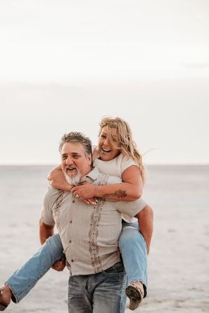 A playful couple shares joyful moments together on a misty beach during a casual photoshoot.