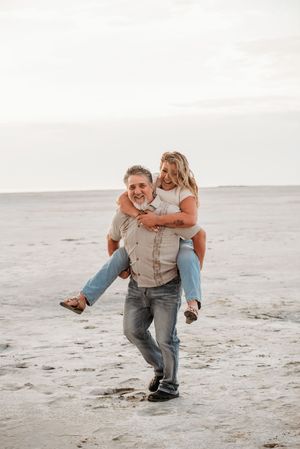 A playful couple shares a piggyback ride moment together on a serene beach at sunset.