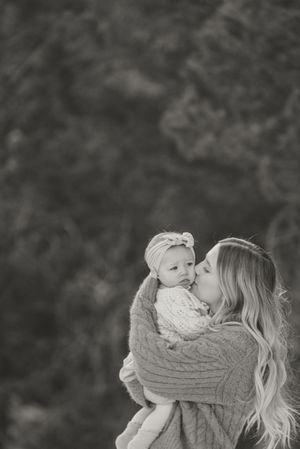 A tender black and white portrait of a mother and baby wearing matching knit sweaters sharing an intimate moment outdoors.