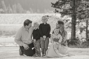 A family of five sits together outdoors in a black and white photograph with mountains and trees in the background.