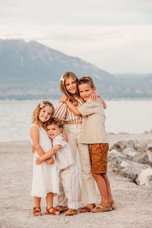 Family portrait session on rocky beach with mountains and water in background during sunset.