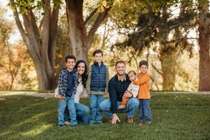 Family sits together on grassy hill during golden hour autumn photoshoot in park.