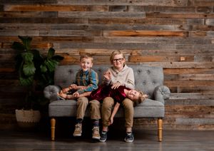 People sitting on a gray couch against a rustic wooden wall in a panoramic view.