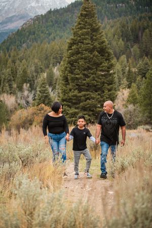 A group walks together through golden sagebrush along a mountain trail surrounded by evergreen forest.