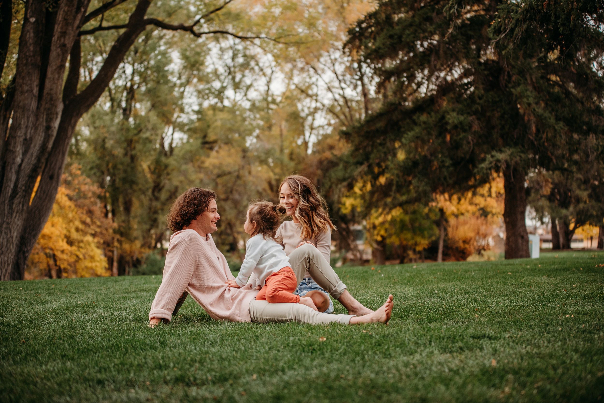 A couple relaxes together on autumn grass surrounded by colorful fall foliage in a park setting.