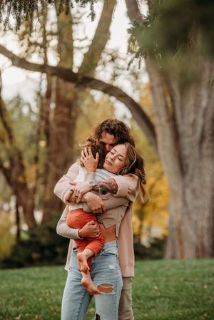 A tender moment between parent and baby in a park during autumn with trees in the background.