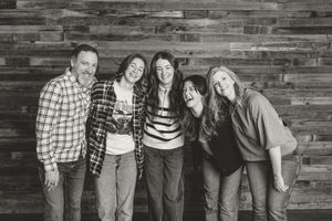 Group photo against rustic wood paneled wall showing casual attire and relaxed poses.