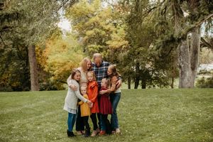 Family group wearing coordinated autumn outfits stands together in a park with fall foliage in the background.