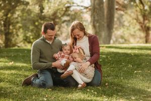 A family sits together on grass in a park during a warm autumn day, sharing tender moments in natural lighting.