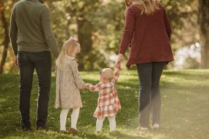 Family walking together in a sunlit park on an autumn day, holding hands in warm earth-tone clothing.