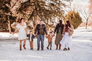 A family walks together through a snowy winter landscape during sunset holding hands in a line.