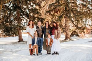 A group gathers under snow-covered evergreen trees for winter outdoor photos in matching earth-tone outfits.