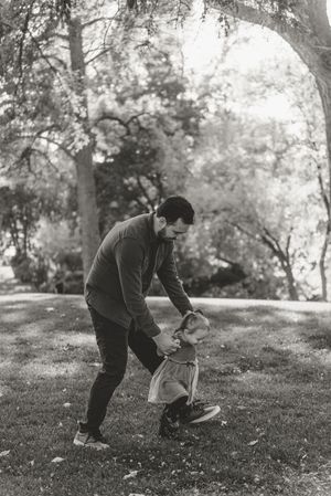 Black and white photo series showing someone in a sweater playing with a small dog on a grassy hill in a park setting.